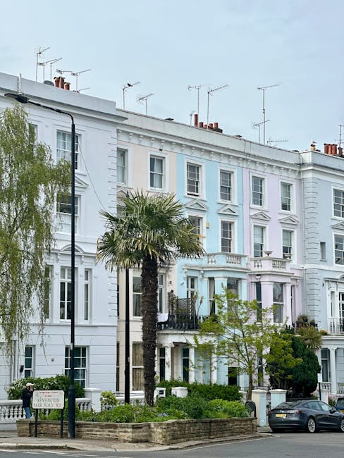Facade of a row of Victorian-style residential buildings in Notting Hill, featuring decorative white and red stucco details, multiple rectangular windows with white frames, some with curtains visible 