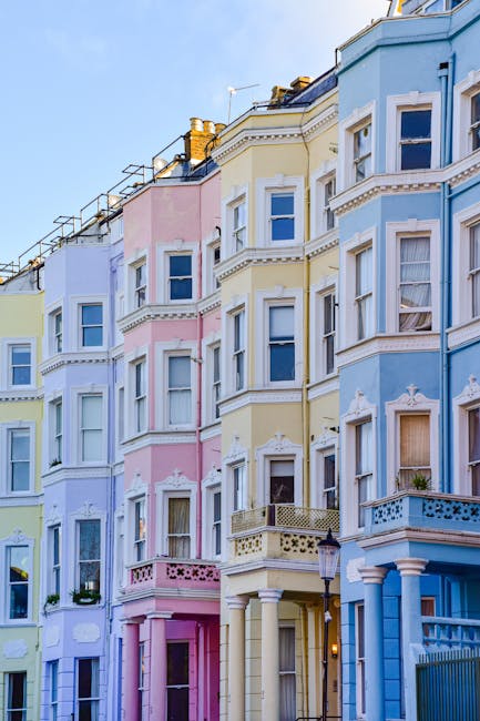 A row of Victorian terraced houses in Notting Hill painted in pastel colors, including turquoise, white, and pink, with bay windows and decorative columns. The buildings feature multiple stories with