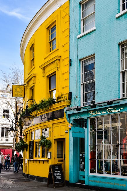 A group of five elderly women and one male waiter are seated around a small outdoor wooden table outside a cafe on a busy street in Notting Hill, London. The women are engaged in conversation, with so